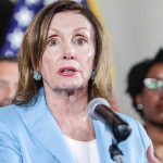 Woman speaking at a press conference with flag behind.