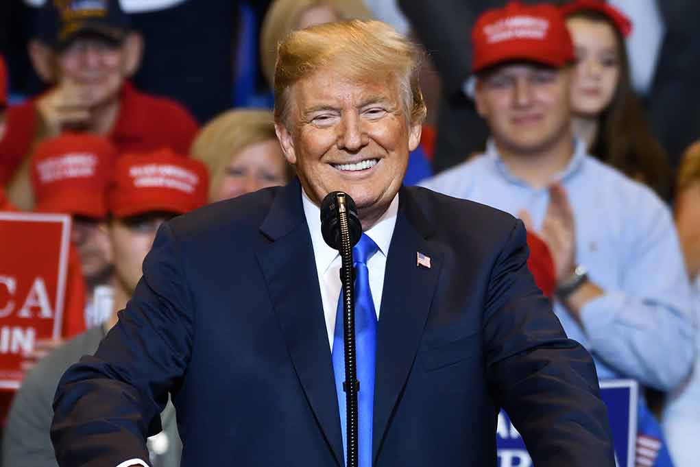 1155247306 featured image Man in suit speaking at rally with red hats.