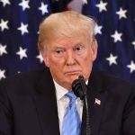 Man speaking at a podium with American flags.