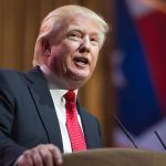 Trump Divides with Johnson on Proxy Voting Issue Man in suit speaking at podium with flag background