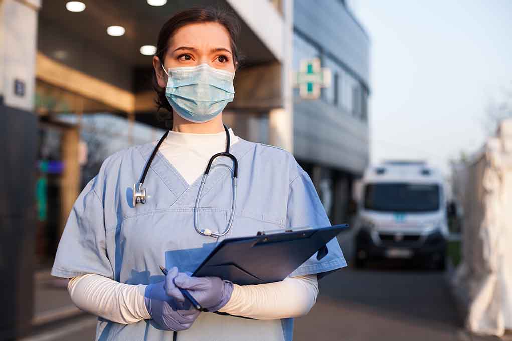 1714681855 featured image Doctor wearing mask and gloves holding clipboard outside hospital