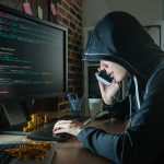 Hacker in hood using computer and phone analyzing code