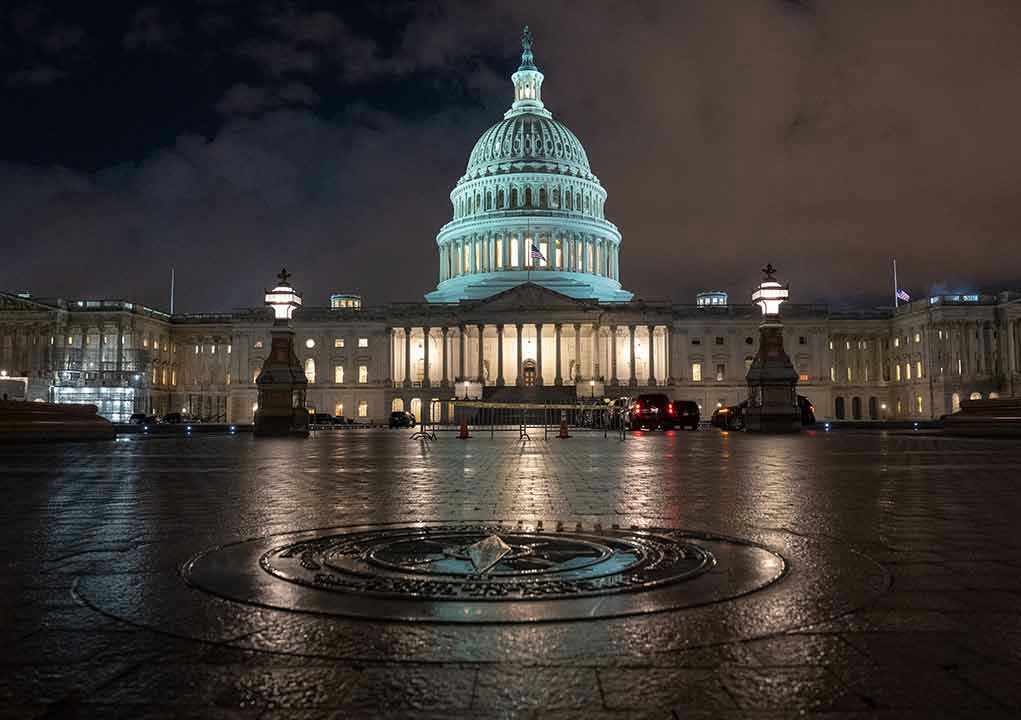 1264598587 U.S. Capitol building illuminated at night with wet pavement.