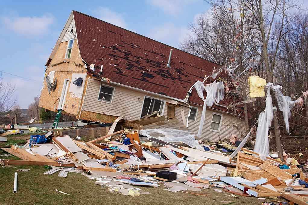 shutterstock_128948774.jpg A severely damaged house tilted on its side surrounded by debris