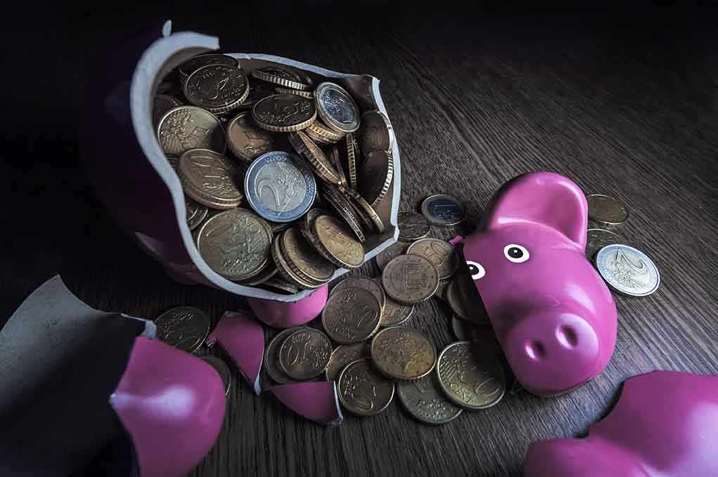 A broken pink piggy bank with coins spilling out onto a wooden surface