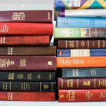 Priest Accused of Fathering a Child With a Stripper Several Bible editions stacked on a bookshelf.