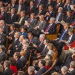 Audience of officials sitting and reading documents in auditorium.