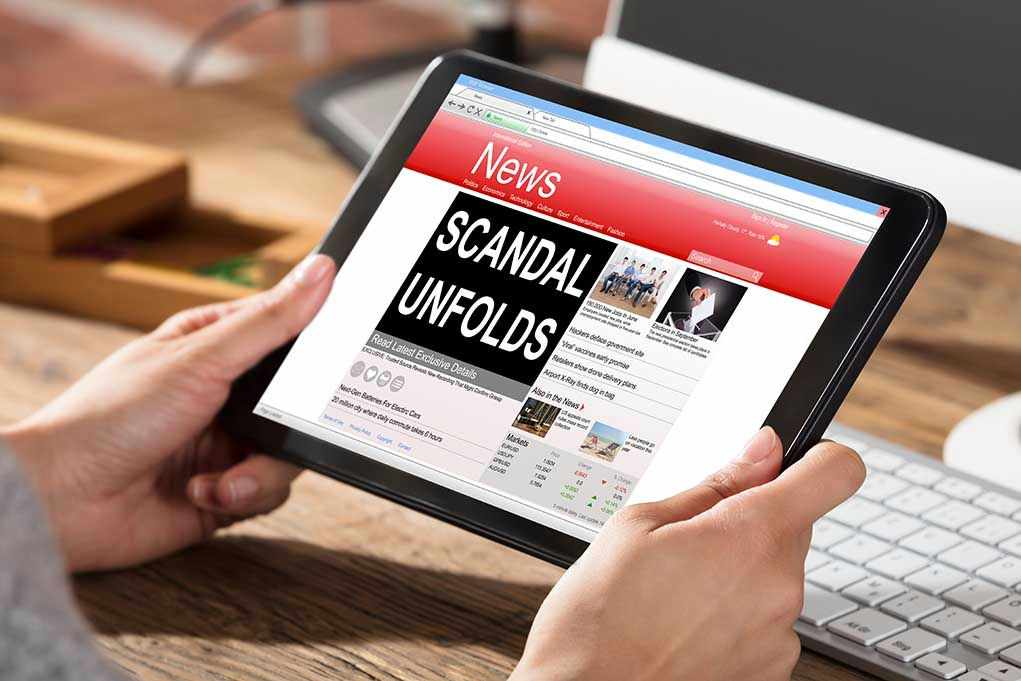 625950956 Person reading news headline Scandal Unfolds on tablet