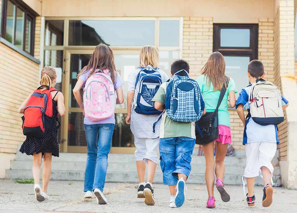shutterstock_167557547.jpg Group of children walking towards a school entrance with backpacks