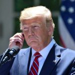 GOVERNOR BLAMES TRUMP – Weaponizes Assassination! Man in a suit adjusting an earpiece.