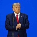 Trump UNLEASHES School Revolution — STANDING OVATION Man in a suit with a blue background.