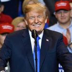 Trump Drops Eric Bomb – Hunter 2.0? Man in suit speaking at rally with red hats.