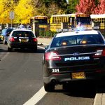 FBI-Police Blitz HALTS School Nightmare – Attack THWARTED! Police cars and school buses on a road.