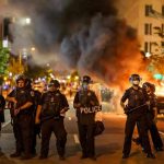Deadly Uprisings EXPLODE Across Two Continents Simultaneously Police officers in riot gear near burning car.