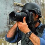 Foreign Diplomatic Crisis—Journalist Held HOSTAGE! Person in helmet taking photos with a large camera.