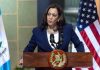 Kamala Sparks Dem Civil War – Even THEY Say No! Person speaking at podium with flags in background.