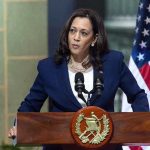 Kamala Sparks Dem Civil War – Even THEY Say No! Person speaking at podium with flags in background.