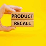 Hand holding Product Recall blocks on yellow background.