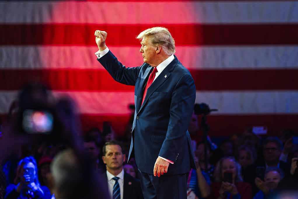 Person in suit with fist raised in front of flag.