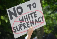 Nazi Uniform Assault – Community REELING! Sign saying No to white supremacy with red circle.