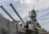 Trump DEPLOYS Fleet – Seen in Attack Formation! Close-up of a battleships naval guns and superstructure against a cloudy sky