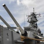 Trump DEPLOYS Fleet – Seen in Attack Formation! Close-up of a battleships naval guns and superstructure against a cloudy sky