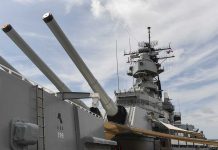 Trump DEPLOYS Fleet – Seen in Attack Formation! Close-up of a battleships naval guns and superstructure against a cloudy sky