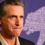 Newsom $450 Million Disaster: Dream Project Implodes Man in suit, solemn expression, purple background with bear drawing.