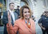 Pelosi’s Mind-Blowing 16,930% – She Made How Much?! Woman in orange blazer speaking, surrounded by security personnel.