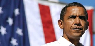 A man in a white shirt standing in front of an American flag