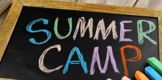 Chalkboard with colorful writing that says Summer Camp and several pieces of chalk