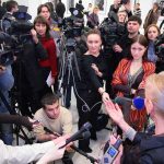 A crowded press conference with journalists and cameras surrounding a speaker