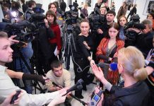 Kirk Widow STUNS Crowd – Mentions Pregnancy! A crowded press conference with journalists and cameras surrounding a speaker