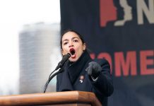 AOC SURGES Ahead of Vance – Stunning Poll Shocker Woman speaking passionately at podium during outdoor event.
