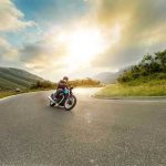 ICONIC Motorcycle Empire CRUMBLES After 122 Years Person rides motorcycle on curved mountain road at sunset.