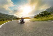 ICONIC Motorcycle Empire CRUMBLES After 122 Years Person rides motorcycle on curved mountain road at sunset.