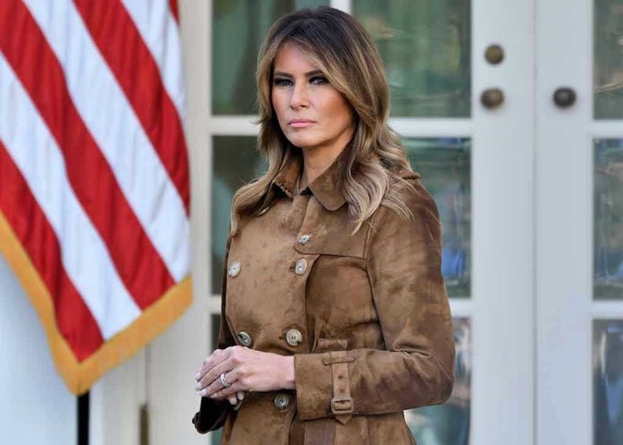 Woman in brown coat beside American flag.