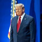 Man in suit next to American flag.
