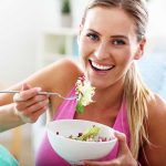 Feel Your Best In 2026: 10 Winter Well-Being Essentials That Can Help Woman smiling and eating a salad bowl.