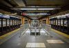 Subway station platform with directional signs overhead.