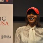 Owens Issues ANOTHER WILD Kirk Theory – Could It Be? A woman wearing a red cap and a white blouse speaking at a political event