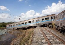 Train CARNAGE – 13 Dead, 98 Injured An overturned train on a railway track surrounded by vegetation