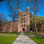 Historic university building surrounded by green grass and trees under a blue sky