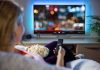 Netflix’s $72B Power Grab Stuns Media World Person sitting on a couch watching a movie on a TV with popcorn in hand