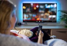 Person sitting on a couch watching a movie on a TV with popcorn in hand