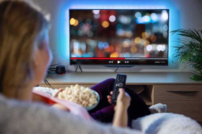 Person sitting on a couch watching a movie on a TV with popcorn in hand