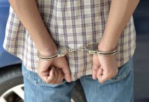 A person in handcuffs viewed from behind, wearing a plaid shirt and denim jeans