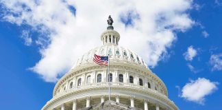 The U.S. Capitol building with an American flag flying in front against a blue sky