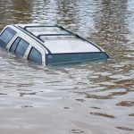 100,000 EVACUATED – Catastrophic Flooding Wrecks State A partially submerged vehicle in floodwaters