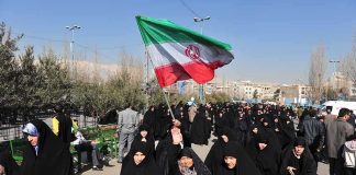 Group of women in black attire marching with an Iranian flag